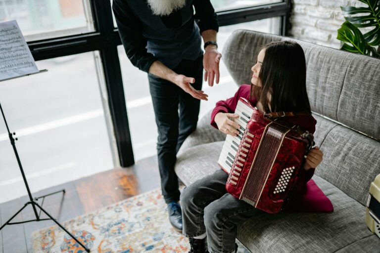 A girl learns to play the accordion with guidance from a music teacher in a cozy indoor setting.
