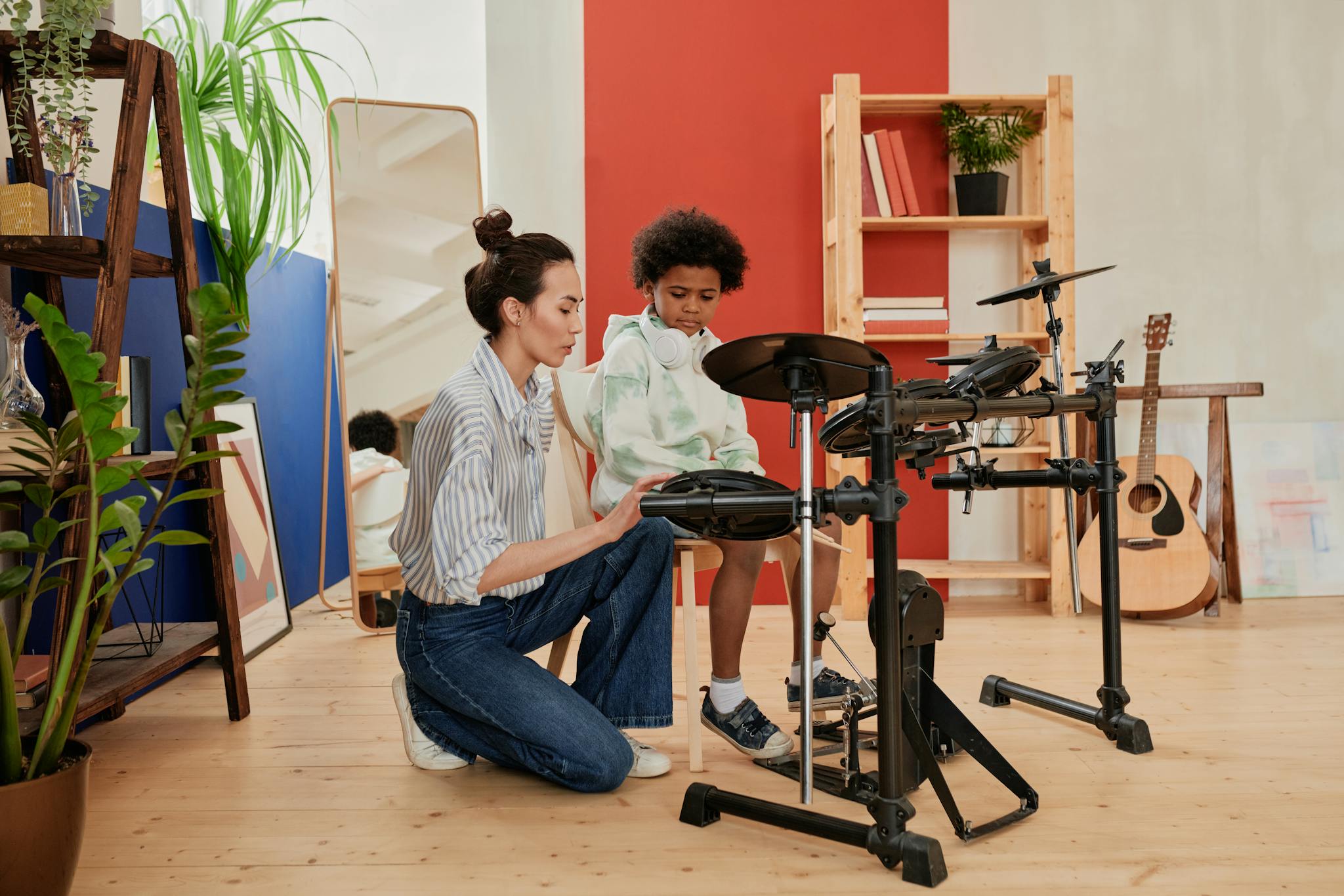 A music teacher guides a child in playing electronic drums in a vibrant studio.